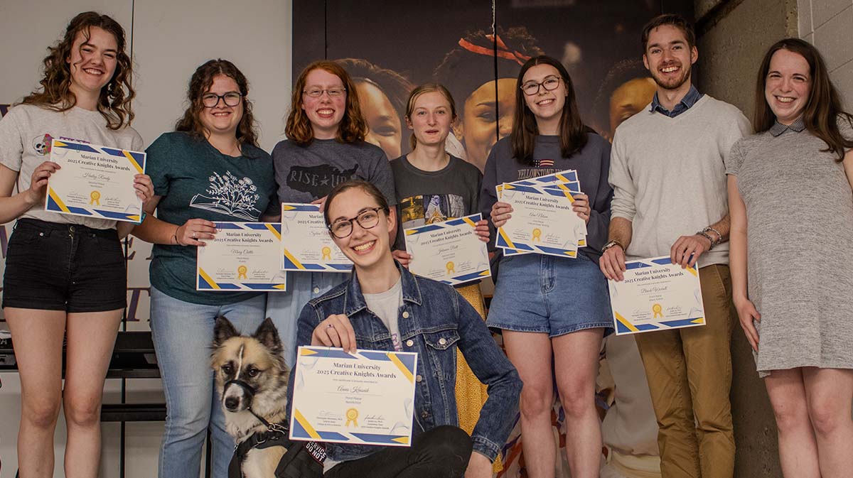 A group of nine young adults proudly displaying their achievement certificates, with one person holding a dog.