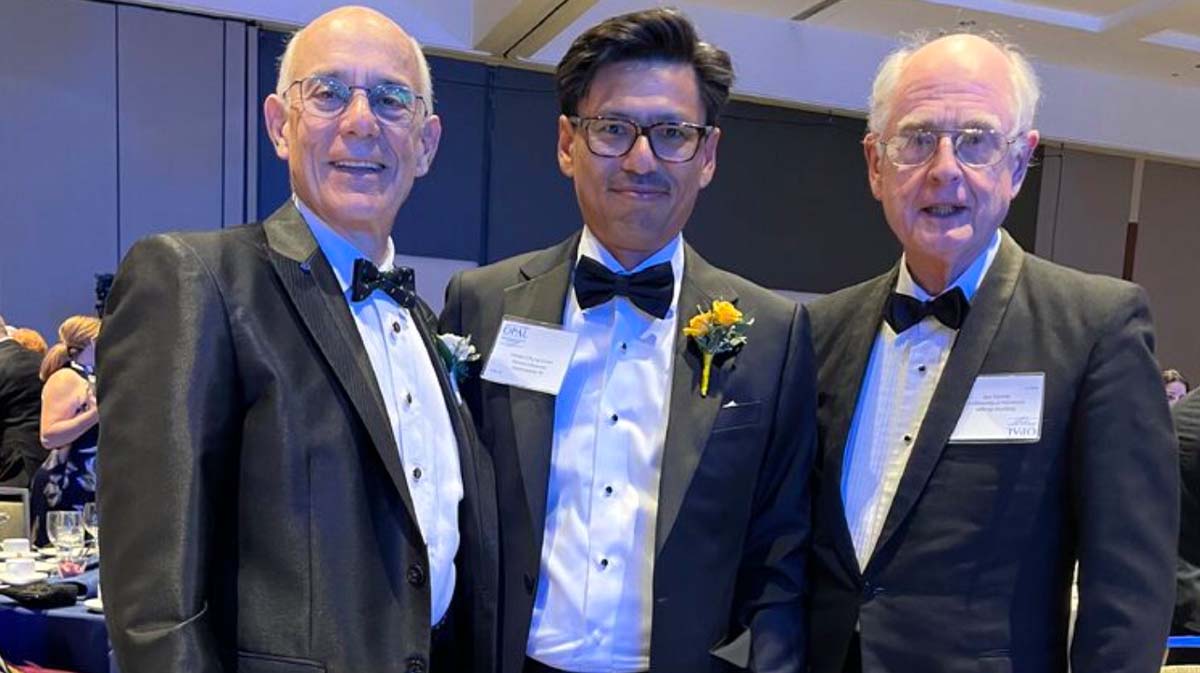 Three men in tuxedos posing together at a formal event, each wearing a bow tie and boutonniere.