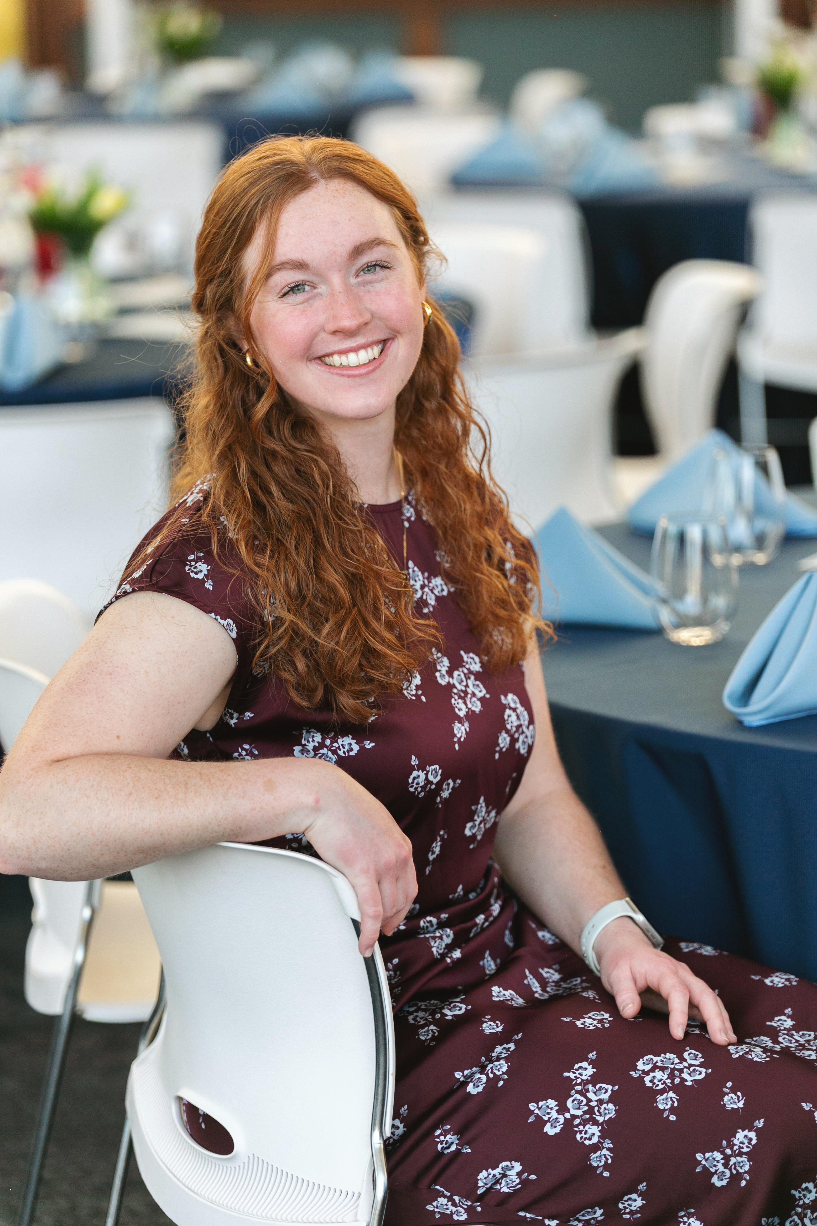 A woman with long red hair smiles while sitting at a beautifully set dining table with blue napkins.