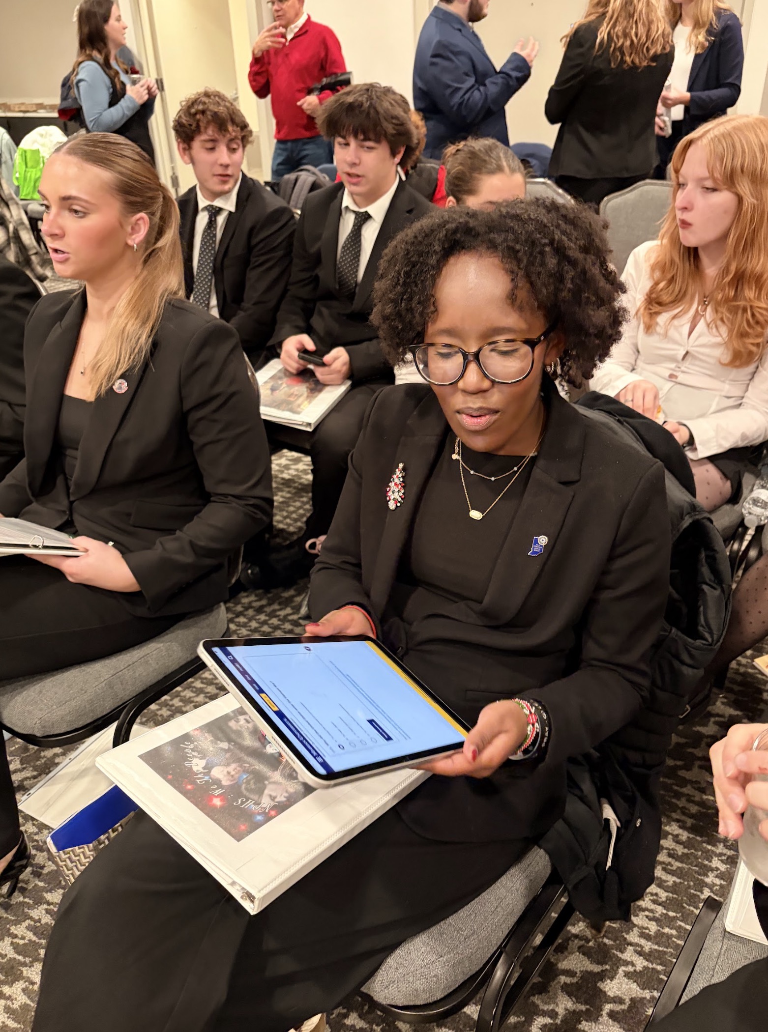 A seated woman with curly hair, focused on her tablet in a professional setting.