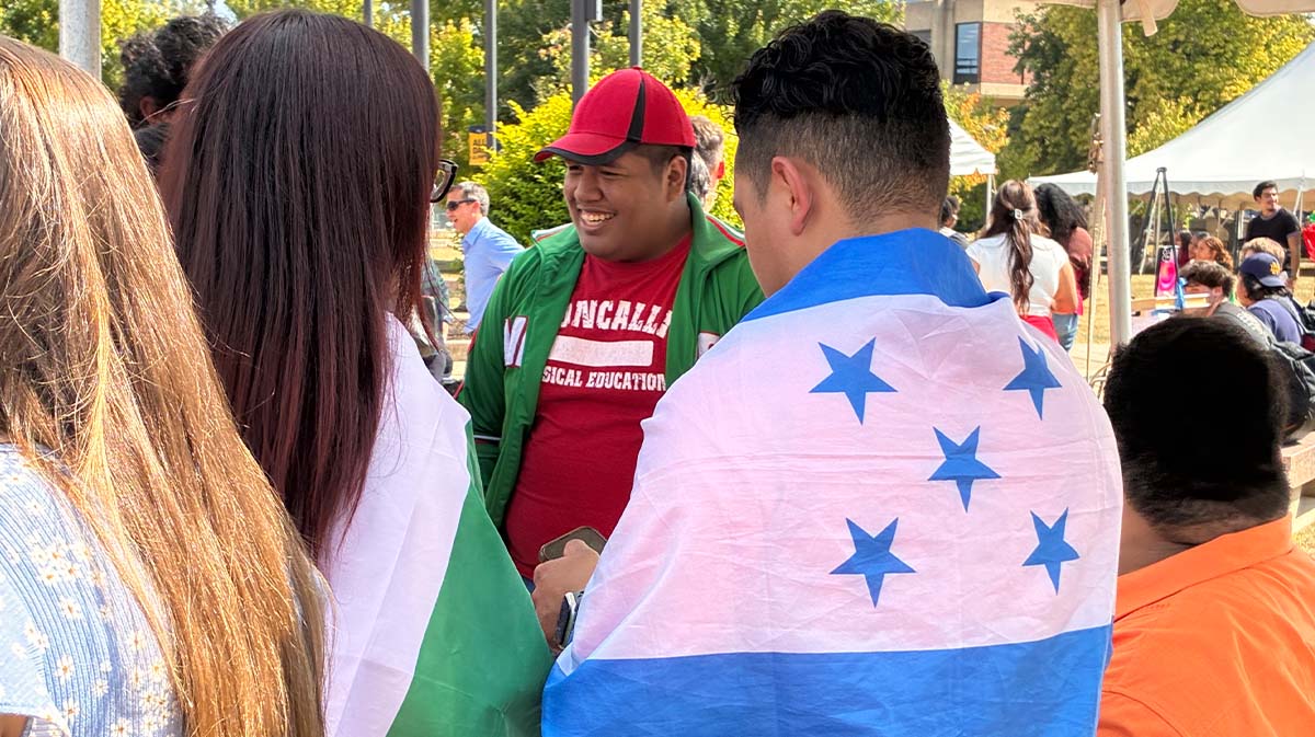 A group of people celebrating cultural diversity, featuring individuals wrapped in flags, including one from Honduras.