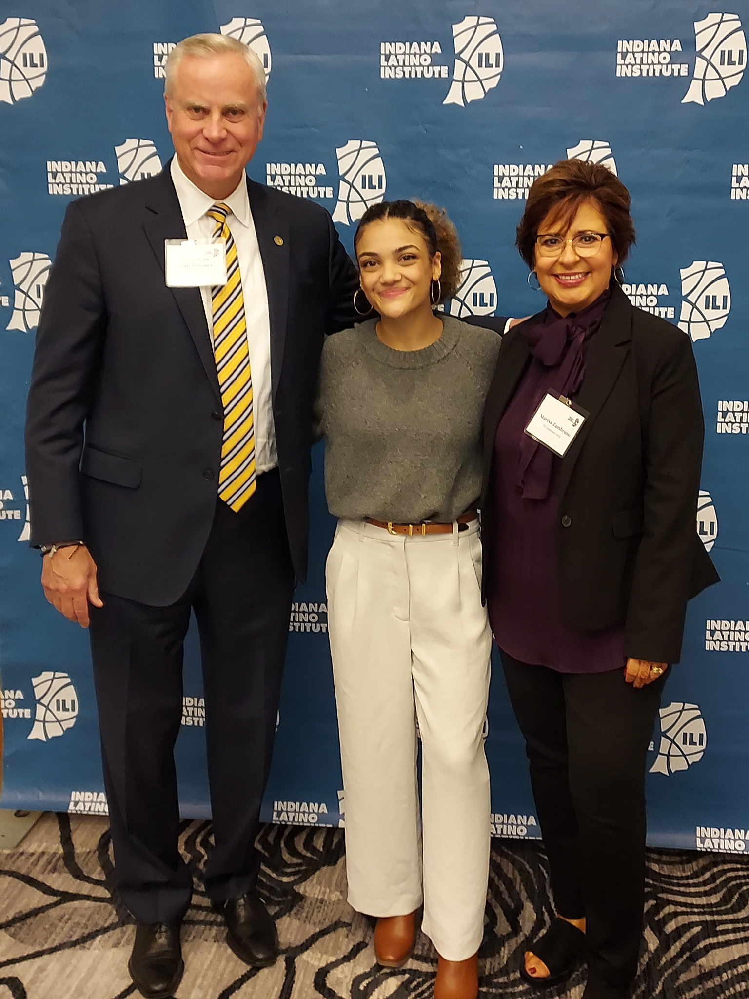 Three individuals pose for a photo at the Indiana Learning Institute event, standing in front of a blue backdrop featuring the institute's logo.