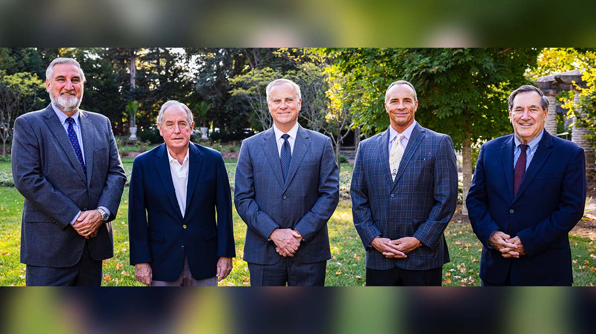 A group portrait of five men standing together outdoors, all dressed in professional attire.