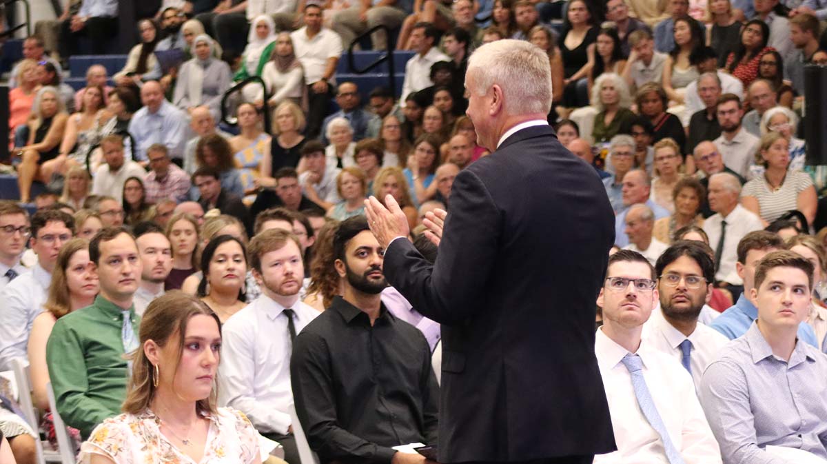President Elsener addresses a large audience during a graduation ceremony, with attendees focused on the presentation.