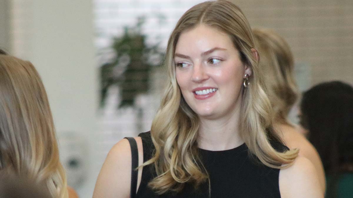 A smiling young woman with long, wavy hair wearing a black top, interacting in a social setting.