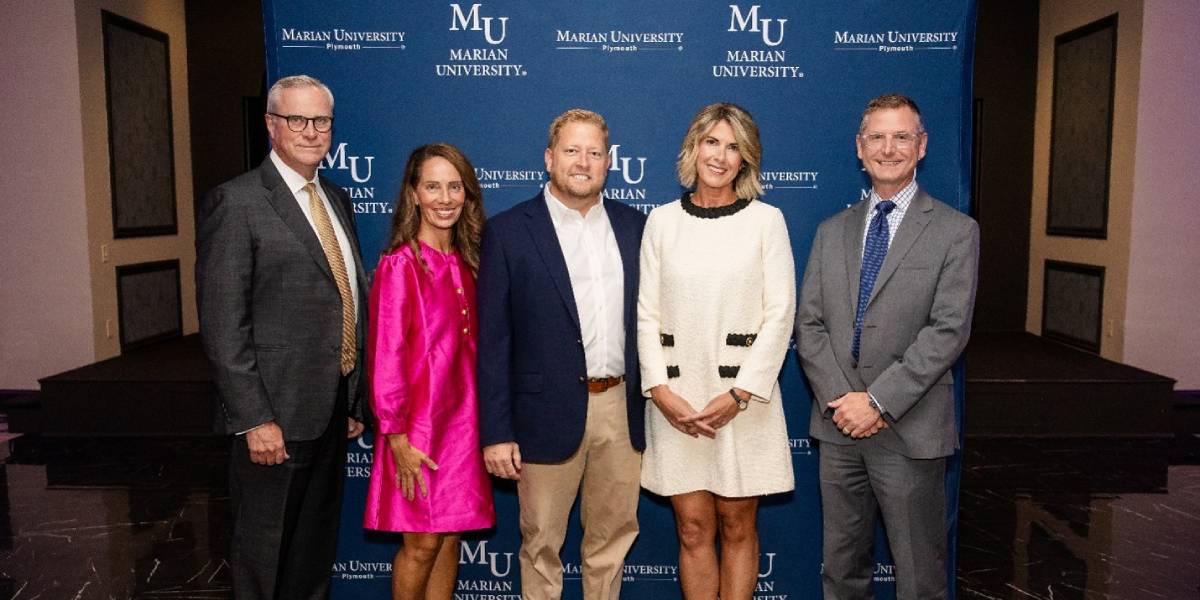 Five people pose for a group photo in front of a Marian University step-and-repeat backdrop at an indoor event.