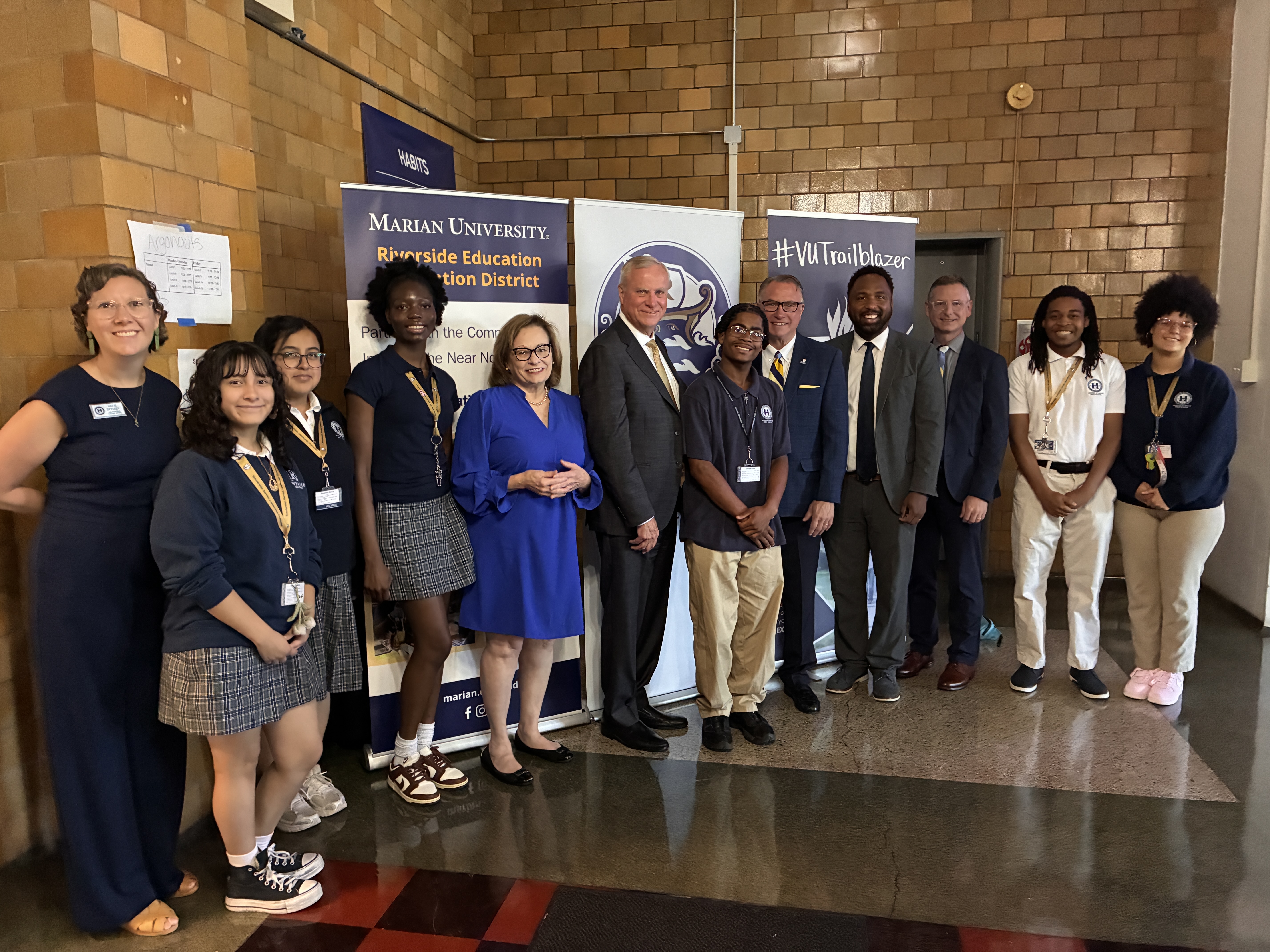 Group of students and educators posing indoors in front of banners for Marian University, Riverside Education, and #VUTrailblazer.