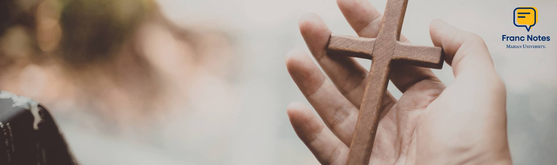 Close up of a hand holding a cross and the Franc Notes logo