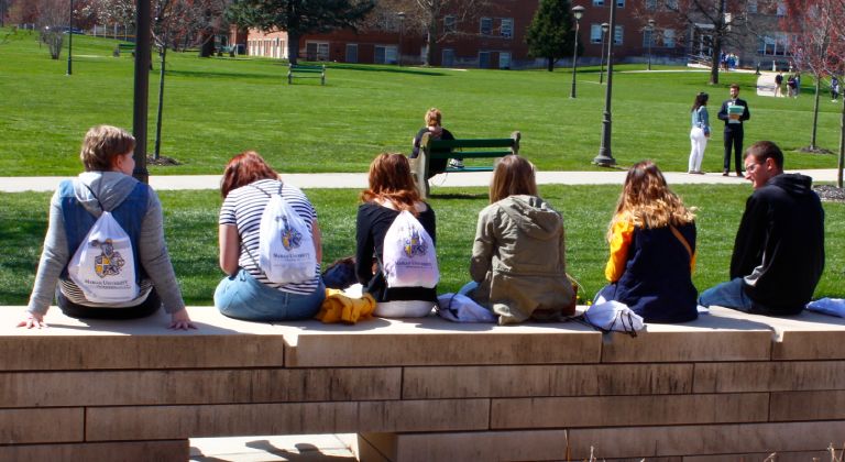 Students sitting on a small brick wall talking