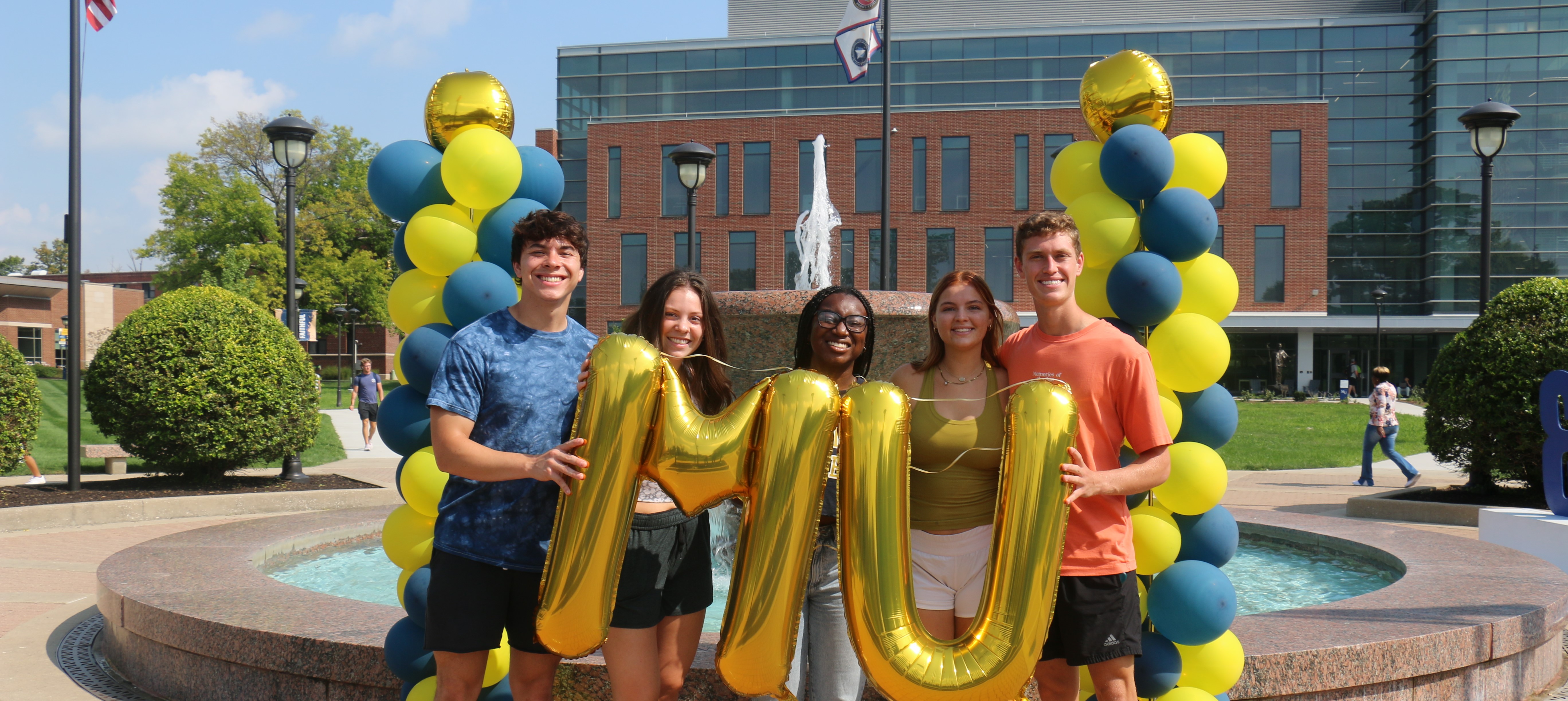 Photo of students holding M U balloons in front of the fountain at Marian University.