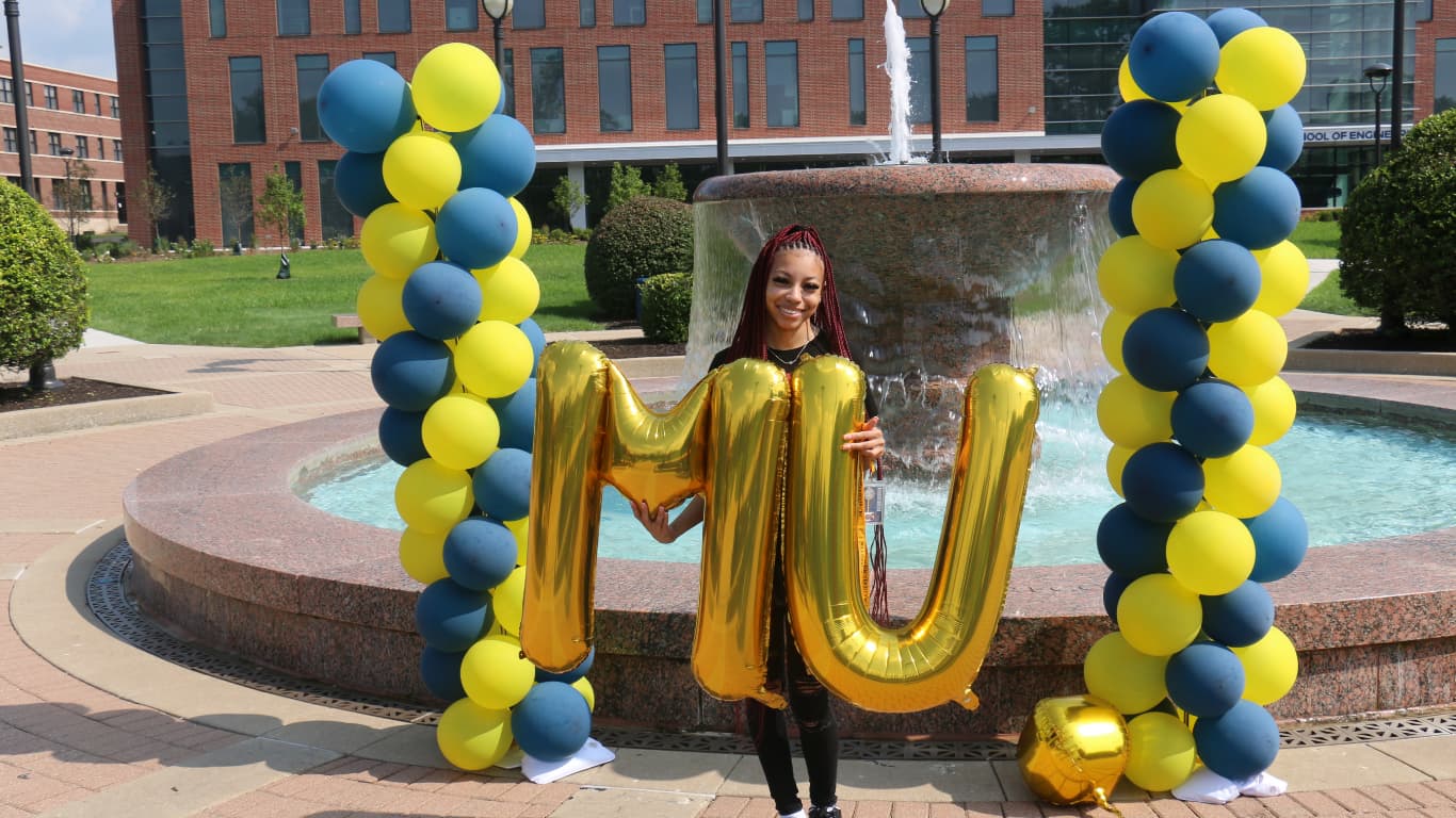 Student holding balloons at water fountain