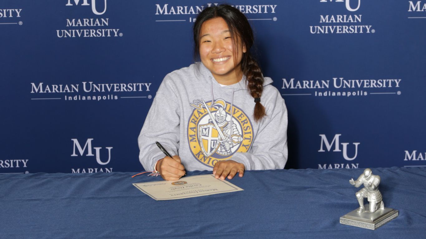 A students smiling for a photo while writing on a paper