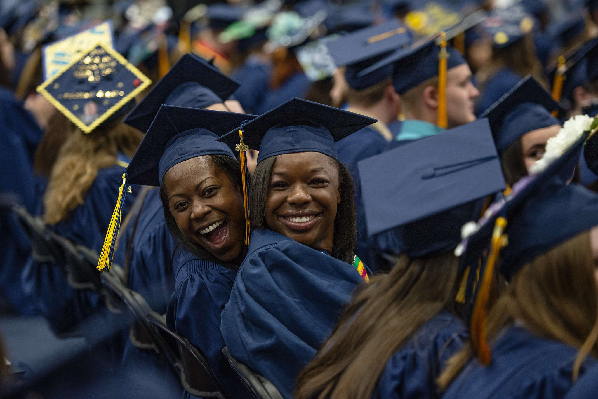 Two joyful graduates in caps and gowns smiling at the camera during a graduation ceremony.