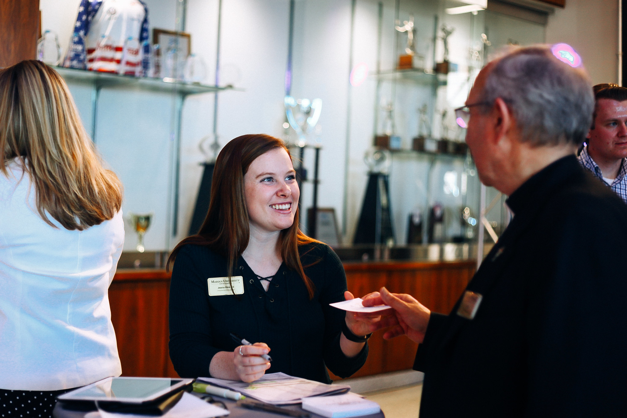 A smiling receptionist interacts with a visitor at a professional event, showcasing a welcoming atmosphere.
