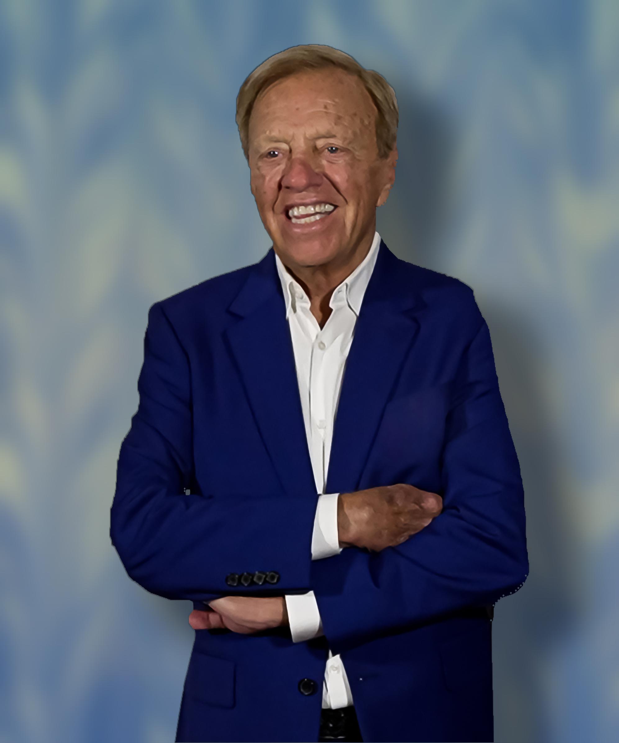 A smiling Michael Leep in a blue blazer stands with his arms crossed, set against a soft blue background.