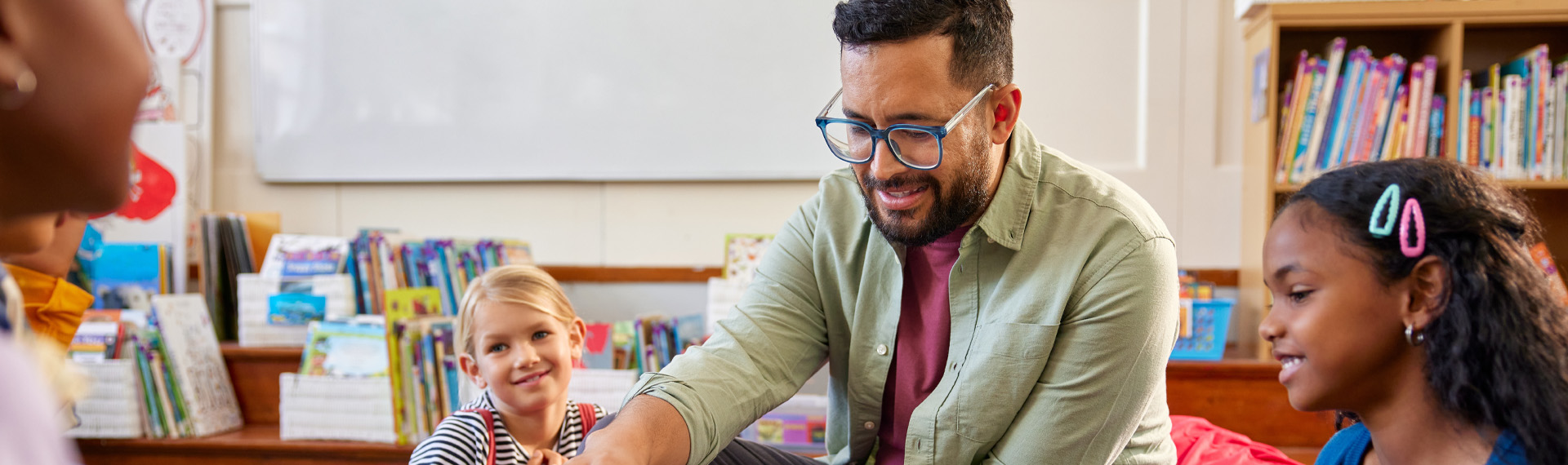 Teacher reading a book aloud to a small group of smiling elementary school children seated on colorful bean bags in a cozy classroom.