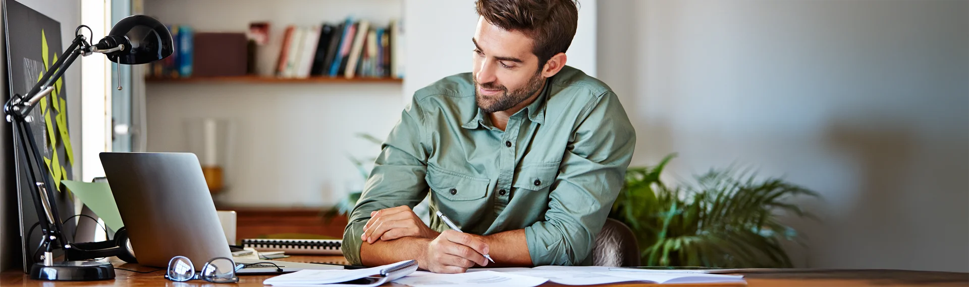 Focused professional man studying at a home office desk with laptop and notes, representing the valuable skills developed in Marian University’s online Logistics degree program