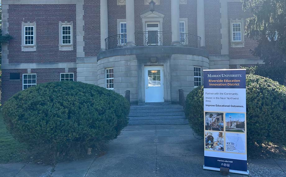 Banner promoting the Riverside Education Innovation District outside Marian University, highlighting community partnership and educational outcomes.
