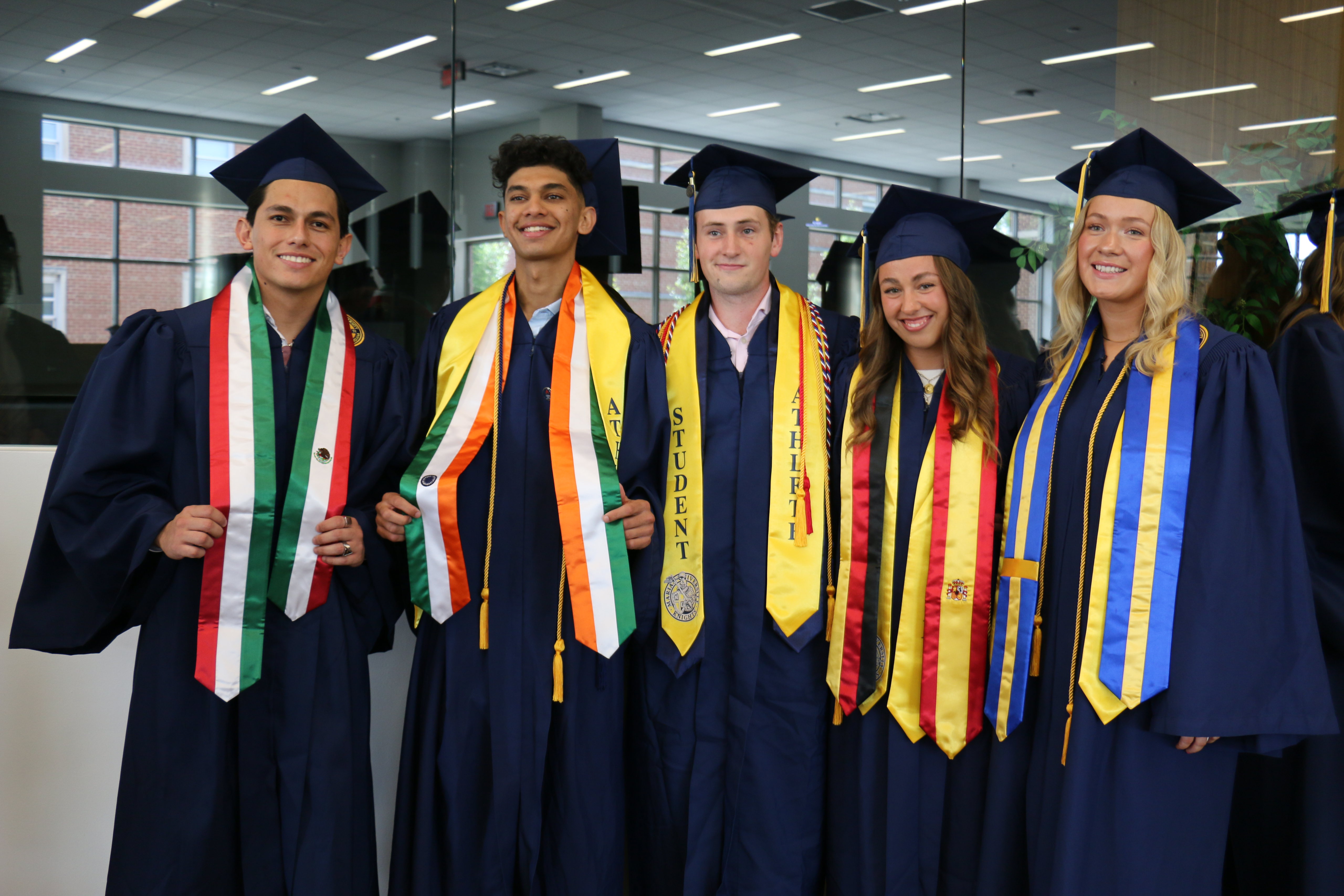 Group of diverse graduates in caps and gowns wearing various honor cords, celebrating their commencement.
