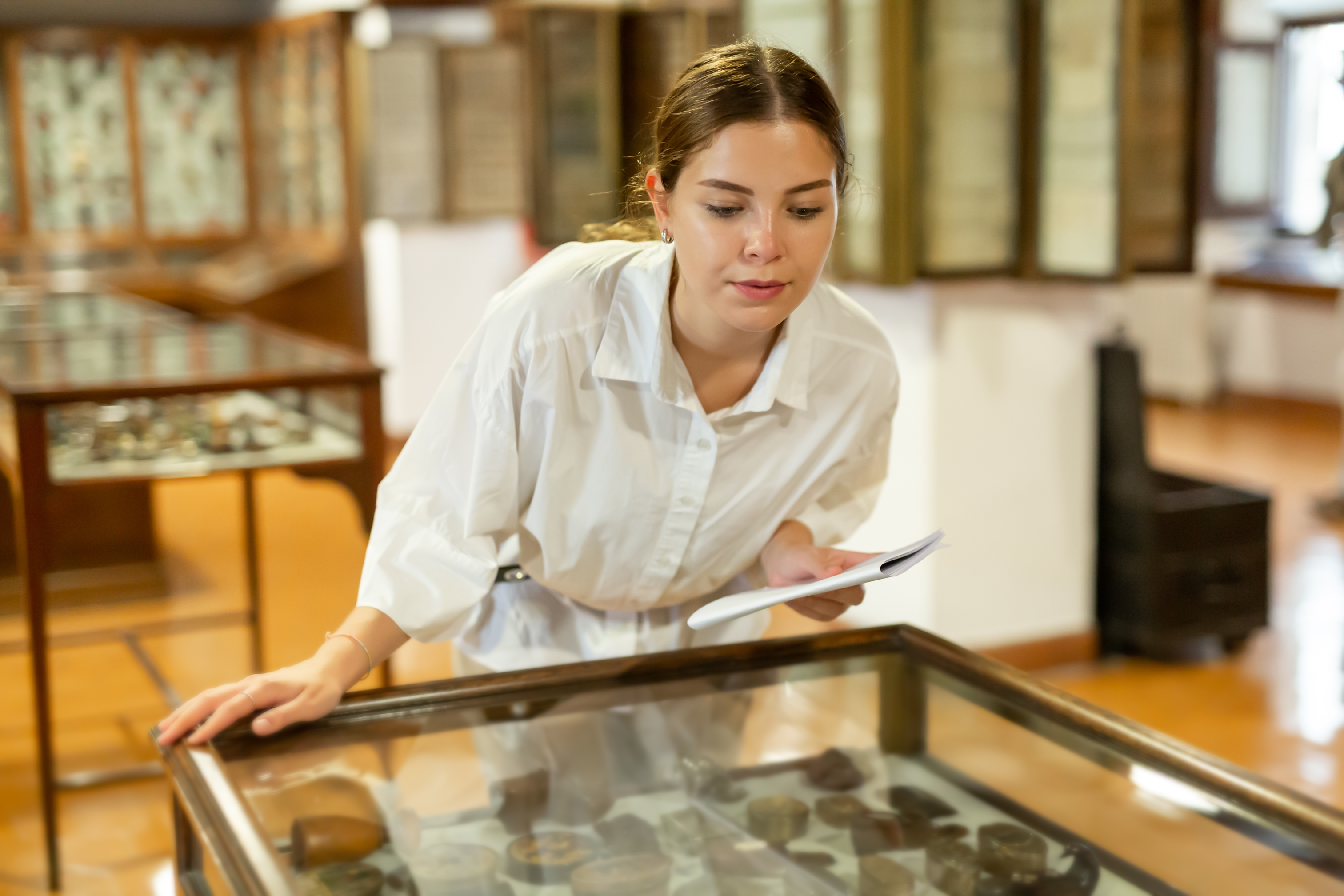 A young woman examining artifacts in a glass display case at a museum.