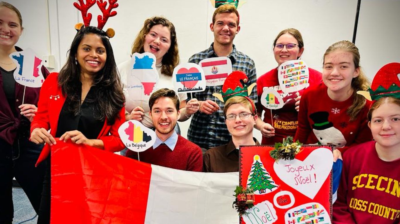 A group of festive students celebrating cultural diversity during a holiday event, wearing Christmas-themed accessories and holding signs representing different countries.