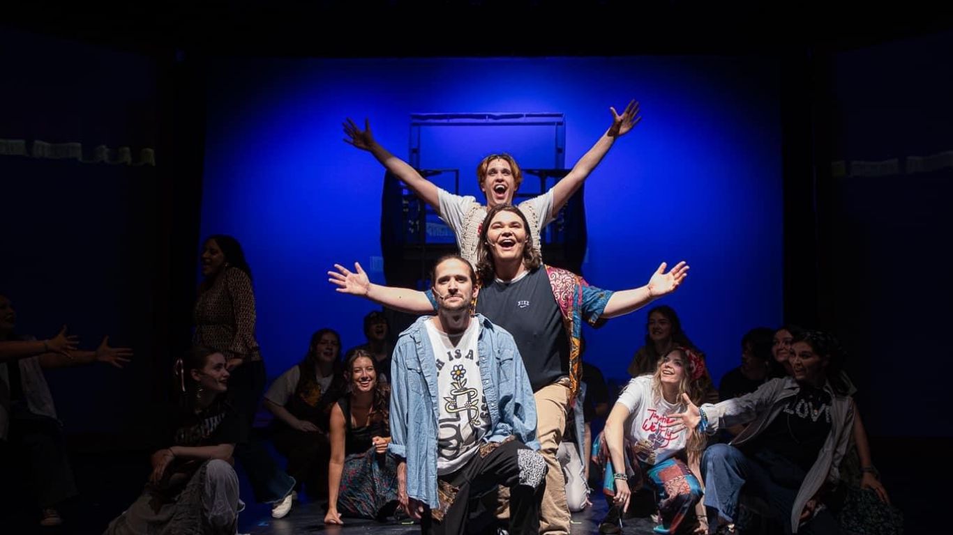 A vibrant theater performance featuring a group of actors in dynamic poses with colorful lighting.