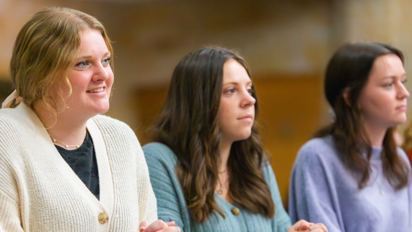 Three young women engaged in a discussion, showcasing diverse expressions and styles in a warm, collaborative setting.