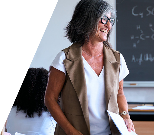 Smiling teacher holding a folder in a classroom, with a chalkboard in the background.