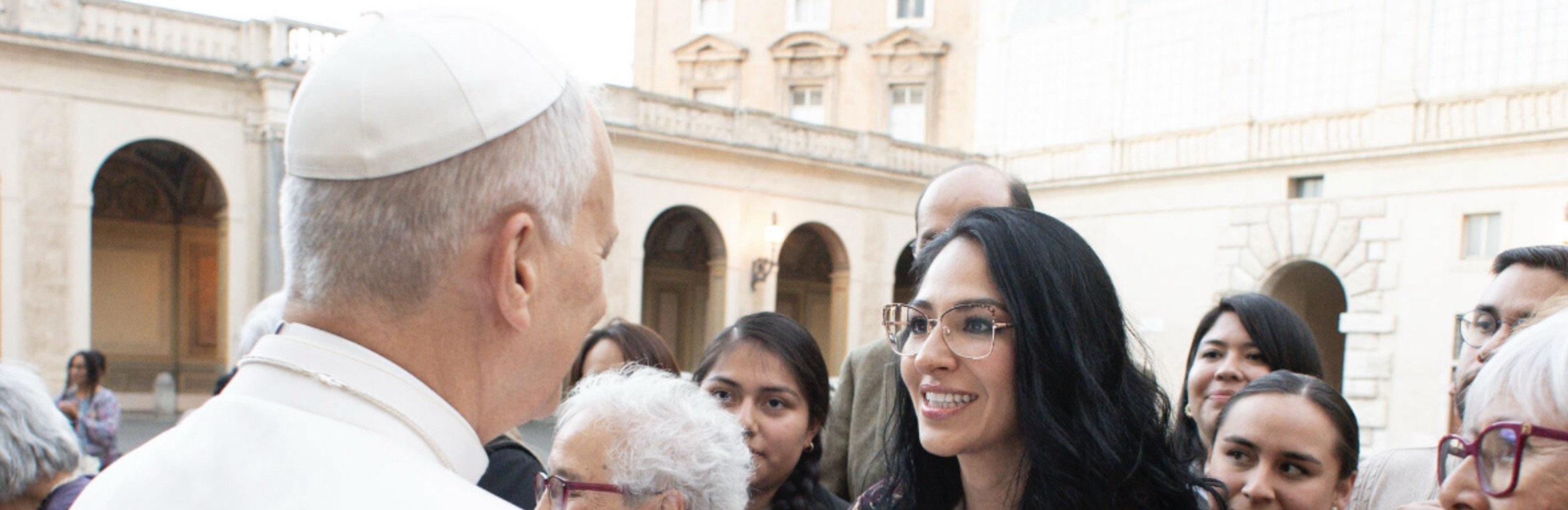 Pope Leo converses warmly with a group of smiling individuals in a historic courtyard.