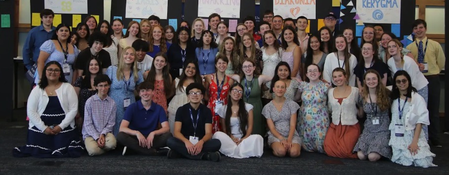Large group of students posing indoors in front of display boards labeled Koinonia, Iasis, Anakrino, Diakonia, and Kerygma.