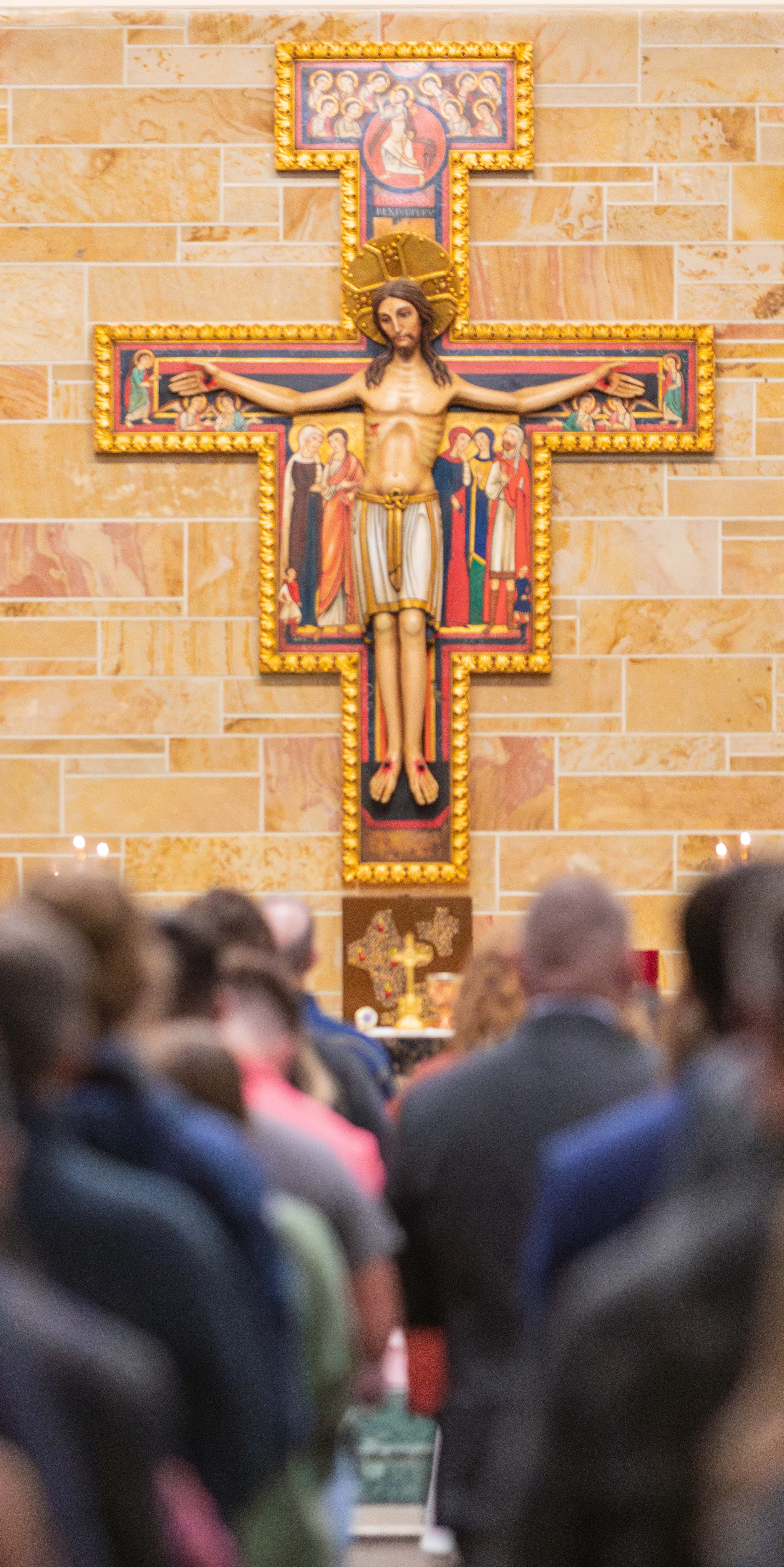 A wooden crucifix depicting Jesus on the cross, surrounded by worshippers in a church setting.