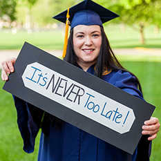 Graduate holding a sign reading &quot;It&#39;s NEVER too late!&quot;