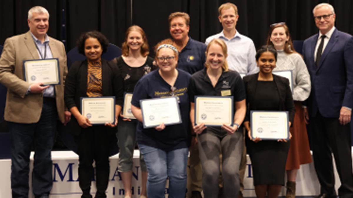 Group photo of award recipients holding certificates at a recognition event.