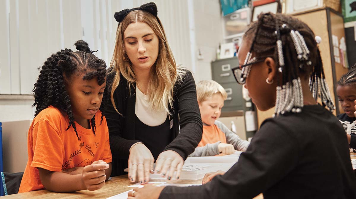 A teacher assists young students during a hands-on learning activity in a classroom setting.