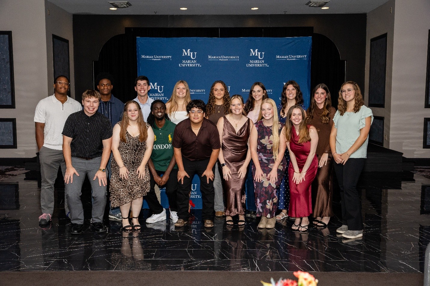 Group of students posing for a formal photo in front of a Marian University (MU) step-and-repeat backdrop.