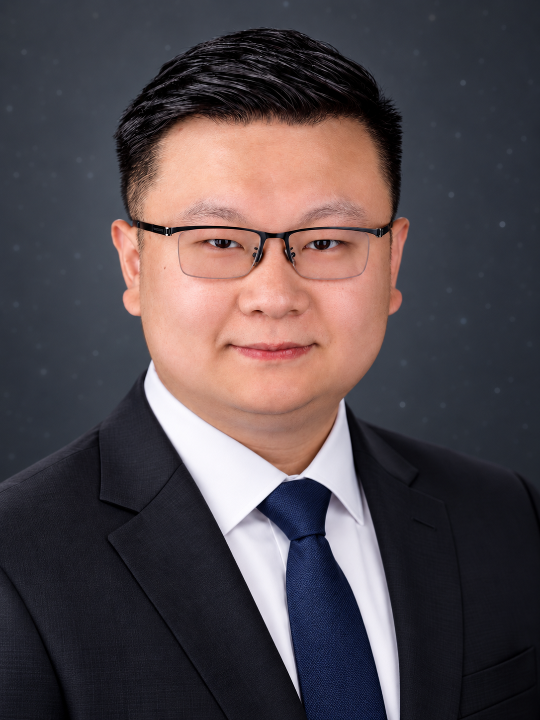 Professional headshot of a person in a dark suit and blue tie, wearing rectangular glasses, against a dark gray backdrop.