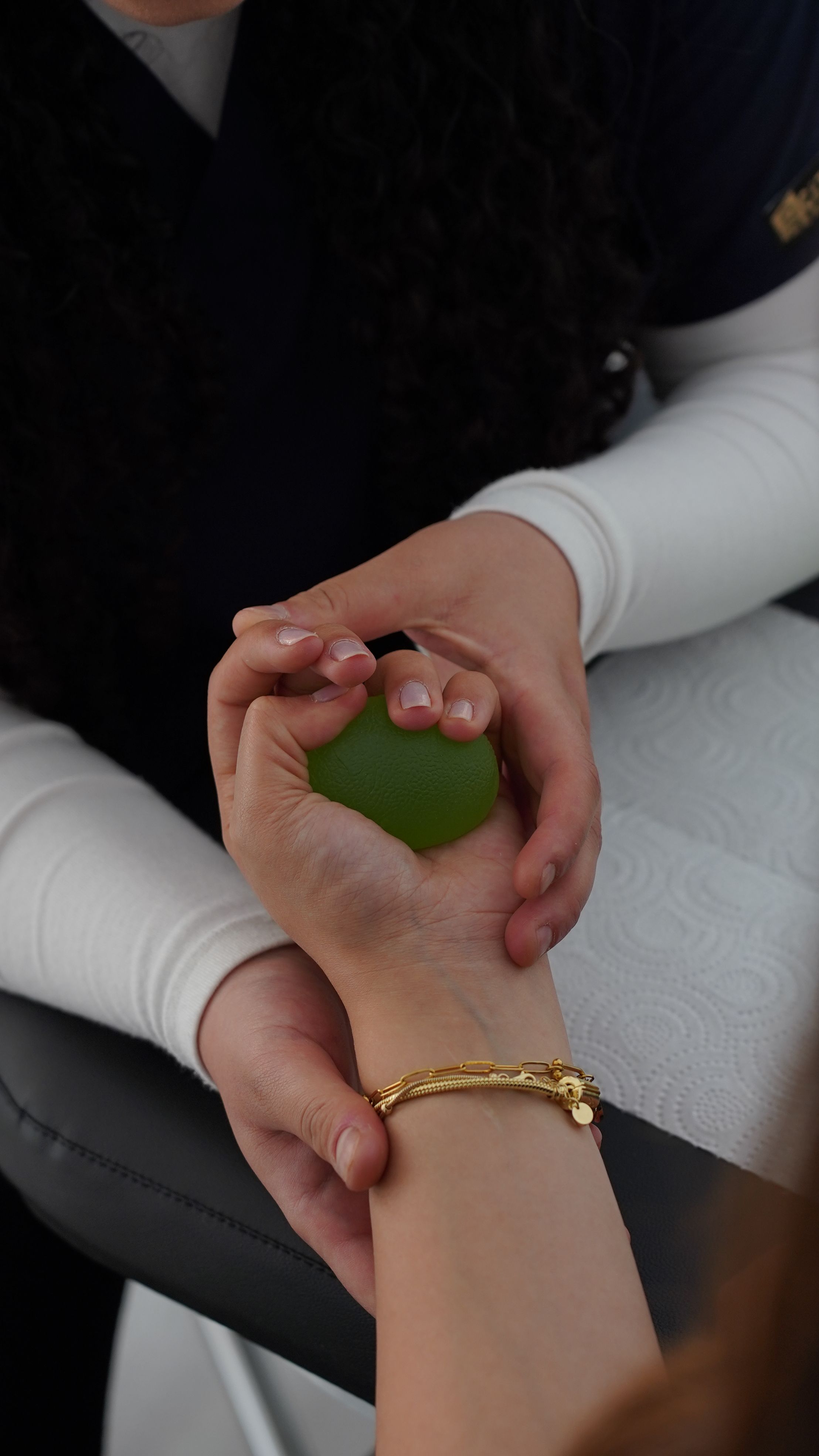 Close-up of two people’s hands, with one person holding the other’s wrist while they squeeze a small green stress ball.