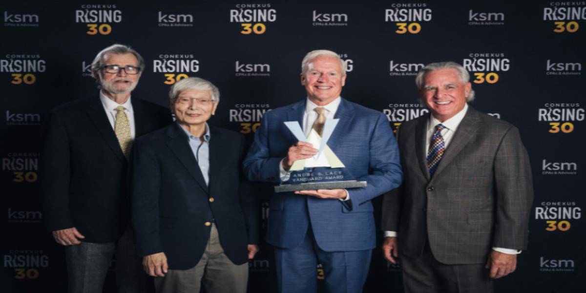 Four men in suits pose at a Conexus Rising 30 event backdrop, with the man in the center holding a glass award.