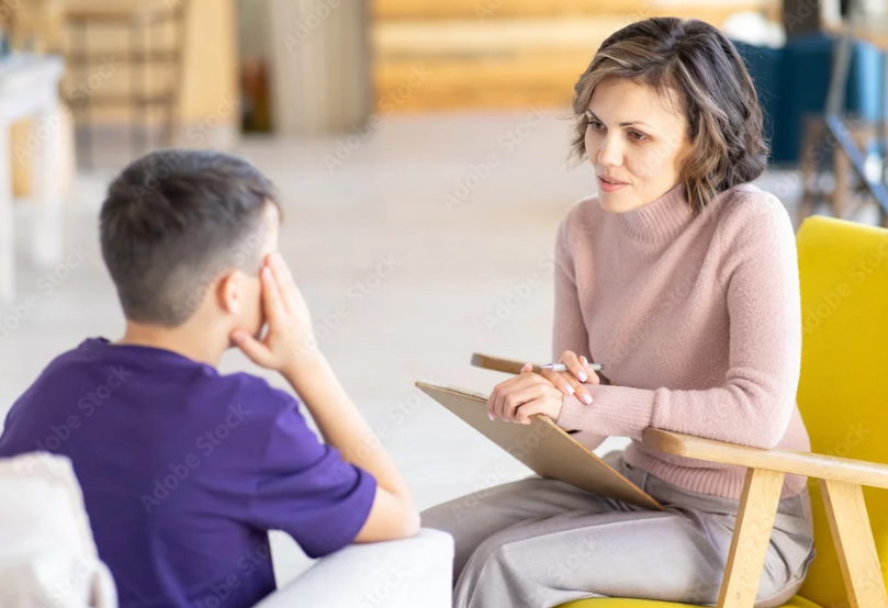 Therapist holding a clipboard and listening to a patient during a counseling session in a bright room.