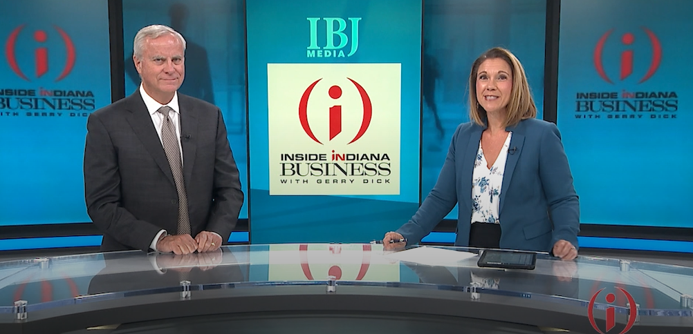 Two news anchors stand behind a studio desk with screens displaying the IBJ Media and Inside Indiana Business logos in the background.